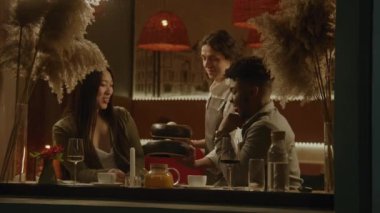 Afrikalı Amerikalı erkek ve Asyalı kadın modern kafede birlikte oturur, şarap içer ve konuşurlar. Erkek garson bulaşık getirir, mum yakar. Restoranda buluşan çok ırklı bir çift. Toplu yemek kavramı.