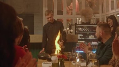 Erkek şef yemeklere alkol döker ve modern gastro kafede insanların önünde flambe tarzında yemek hazırlar. Doğum günü partisinde bir grup arkadaş, geceyi restoranda geçirirler. Toplu yemek kavramı.