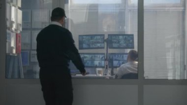 Güvenlik görevlisi iş arkadaşı olarak odaya girer. Güvenlik operatörü CCTV kameralarını izliyor, telsiz ve güvenlik kamerası görüntülerini gösteren ekranlı bilgisayarlar kullanıyor. Yüksek teknoloji güvenlik kavramı.