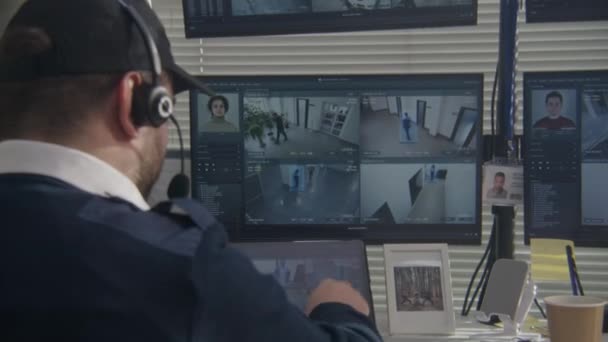 ヘッドセットのセキュリティ担当者は 監視室でコンピュータ上のCctvカメラを監視します Ai顔認識ハイテクソフトウェアを搭載した監視カメラの映像を示す複数のPc画面 バックビュー — ストック動画