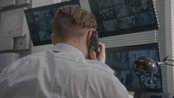 監視室で固定電話で警備員が話をする セキュリティ担当者は コンピュータ上のCctvカメラを監視します 顔認識ソフトウェアでセキュリティカメラの映像を示す画面 バックビュー — ストック動画