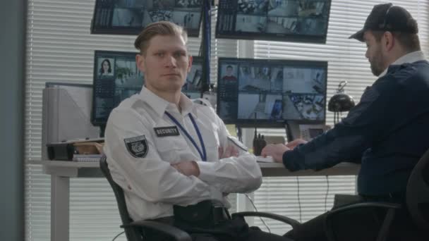 警備員が監視室に座り カメラを見ている 同僚は コンピュータの複数の画面上のCctvカメラ映像をバックグラウンドで監視します Ai顔認識システムを搭載したハイテクソフトウェア — ストック動画