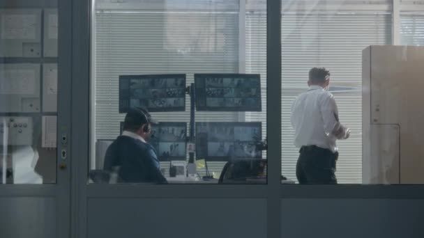 警卫人员通过观察室的百叶窗向窗外望去 然后与同事一起监视显示在电脑屏幕上的闭路电视摄像头 观测和跟踪系统 社会安全 — 图库视频影像