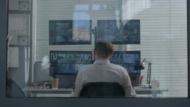 警備員は監視室に座り 椅子の後ろにもたれている セキュリティオペレータは 最新のソフトウェアを使用してコンピュータモニタに表示されるCctvカメラを制御します 観測技術 バックビュー — ストック動画