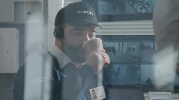 ヘッドセットの警備員はコーヒーや紅茶を飲み 同僚と話をします Pc画面にAi顔スキャンが表示されたCctvカメラからの眺め ハイテク観測とセキュリティシステム 肖像画 — ストック動画