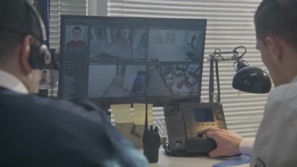 ヘッドセットの男性オペレーターは コンピュータ上のカメラを監視し コーヒーを飲みます 警備員は固定電話を使う 顔認識ソフトウェアでCctvカメラ映像を示す複数の画面 閉じろ — ストック動画