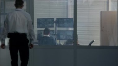 Üniformalı güvenlik görevlisi gözlem odasına giriyor, meslektaşlarıyla masaya oturuyor ve bilgisayar ekranlarında görüntülenen CCTV kameralarını izliyor. Modern güvenlik sistemi. Sosyal güvenlik kavramı.