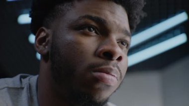 Afro-Amerikan genç bir adamın detaylı portresi. Düzgün ve ciddi bir yüzü var. Kendine güveni tam. Yoğunlaşmış adam başka tarafa bakıyor, gözlerini kırpıyor, kameraya poz veriyor. Adam stüdyoda duruyor. Arka planda LED lambaları.