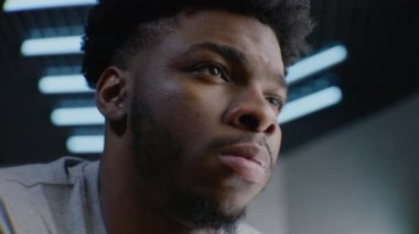 Genç, Afro-Amerikalı, kendine güvenen ve ciddi bir yüzü olan bir adam. Odaklanmış adam gözlerini kırpıyor, kameraya poz veriyor. Adam stüdyoda duruyor. Arka planda LED lambaları var. Portreyi kapat.