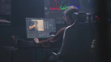 Kadın editör, modern stüdyoda profesyonel kurgu yazılımı kullanarak bilgisayar üzerinde çalışıyor. Kadın video görüntülerini düzenliyor, film sonrası film için renk değerlendirmesi yapıyor. RGB grafikli büyük ekran.