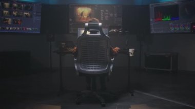 Video yapımcısı stüdyoda bilgisayar üzerinde çalışıyor, video düzenliyor, film sonrası film için renk değerlendirmesi yapıyor. Film görüntüleri, RGB grafikleri ve seviyeleri ile renk düzenleme programı arayüzünü gösteren büyük ekranlar.