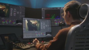 Editör stüdyoda bilgisayarda çalışıyor, renk derecelendirme kontrol paneli kullanıyor, video düzenliyor, film için renk düzeltmesi yapıyor. Program arayüzünü gösteren büyük ekranlar film görüntüleri, RGB grafikleri ve seviyeleri