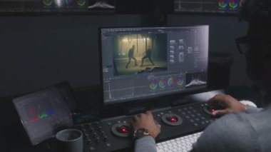 Afrikalı Amerikalı film editörü modern stüdyoda kontrol yüzeyine renk notu veriyor. Büyük ekranlarda film görüntüleri ve duvarında RGB renk düzeltme çubuğu var. Video post prodüksiyon süreci.