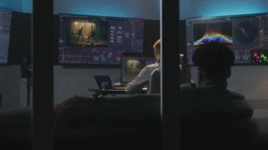 Çok ırklı renk bilimciler ve film yapımcıları filmi düzenler ve profesyonel yazılımda renk sınıflandırması yaparlar. Stüdyodaki video prodüksiyonunun renk düzeltme süreci. Aksiyon filmi görüntülü ekranlar.