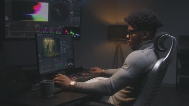 アフリカ系アメリカ人の映画製作者は 現代のスタジオでコンピュータ上でカラーグレーディングを行う 壁にRgbカラー補正グラフィックバー付きの大きな画面 モニターに表示されるアクションフィルム映像 カラーリスト装置 — ストック動画