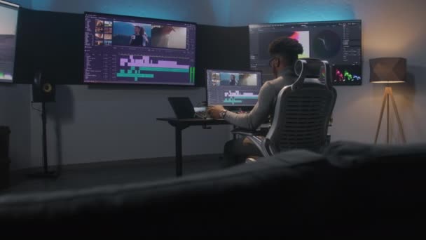 非裔美国人多媒体艺术家喝咖啡 并在计算机编辑程序中进行色彩分级 在现代演播室进行视频后期制作的过程 带有旅行电影镜头的多个监视器 — 图库视频影像