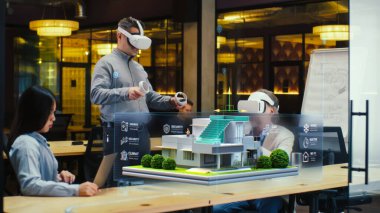 Erkek tasarımcı sanal gerçeklikte iş arkadaşlarına akıllı ev tasarım projesini sunan VR kulaklık ve kablosuz kontrol cihazları kullanır. Modern yüksek teknoloji şirketi. Üç boyutlu hologram. Gelecekteki dijital teknolojiler.