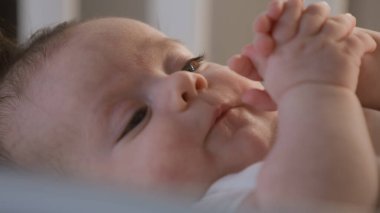 Beyaz takım elbiseli beyaz çocuk portresi sabahları beyaz çarşaflarla beşikte yatar. Sevimli ve tatlı çocuk elleriyle oynuyor. Bebek, çocukluk, ebeveynlik, hayat ve aile kavramı.