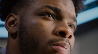 Afro-Amerikalı genç bir adamın portresi. Kendine güvenen ve derin bakışlı ciddi bir yüz. Yoğunlaşmış adam başka tarafa bakıyor, gözlerini kırpıyor, kameraya poz veriyor. Adam stüdyoda duruyor. Arka planda LED lambaları var. Kapat..