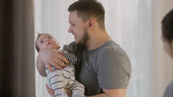 stock image Man lulls newborn baby in bodysuit before day nap at nursery. Caring father holds sweet baby daughter or son in his arms, smiles and talks with wife. Concept of childhood, parenthood, family and love.