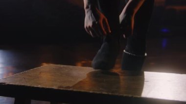 Antrenman kıyafetli erkek balerin koreografi provasına hazırlanırken bale ayakkabısı giyer. Adam gösteriden önce tiyatro sahnesinde ısınma egzersizleri yapmaya başlıyor. Klasik bale dansı..