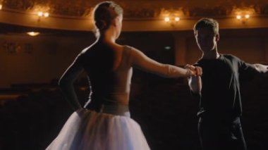 Seçkin bale dansçıları koreografi provası sırasında tiyatro sahnesinde bale hareketleri yaparlar. Erkek ve kadın pratik yapar ve dans gösterisine hazırlanırlar. Klasik bale sanatı. Dramatik ışıklandırma.