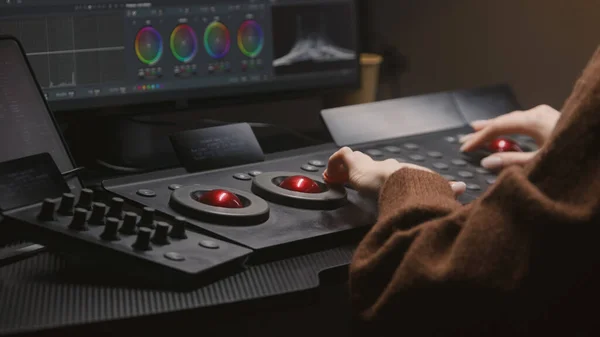 Female editor works in studio, uses digital color grading control panel. Colorist makes video color correction on computer. Program interface with RGB graphics, color wheels and levels on PC monitor.