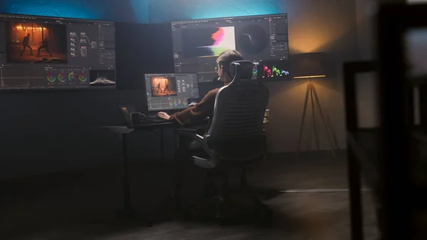 Female film editor or colorist does color grading on computer in modern studio. Big monitors with RGB colour correction graphic bar and program interface on the wall. Video post production. Handheld.