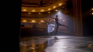 Graceful ballerina dances with partner in training suit and rehearses choreography moves on theater stage. Couple of ballet dancers practice before performance. Classical ballet art concept. Handheld. clipart
