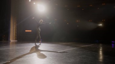 Sahnede sahne ışıklarıyla aydınlatılan kadın dansçı. Antrenman kıyafetli balerin, koreografi provasında zarif bale hareketleri yapıyor. Modern bale sanatı.