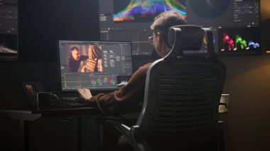 Kadın editör, modern stüdyoda profesyonel kurgu yazılımı kullanarak bilgisayar üzerinde çalışıyor. Kadın video görüntülerini düzenliyor, film sonrası film için renk değerlendirmesi yapıyor. RGB grafikli büyük ekran.