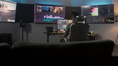 Afrikalı Amerikalı multimedya sanatçısı kahve içiyor ve düzenleme programında renk değerlendirmesi yapıyor. Modern stüdyoda video prodüksiyon süreci. Seyahat filmi görüntüleriyle birden fazla monitör.