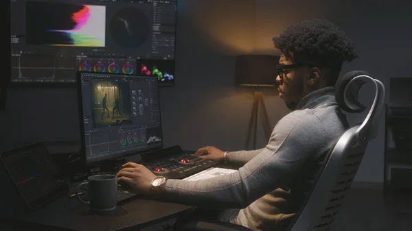 African American film maker makes color grading on computer in modern studio. Big screen with RGB colour correction graphic bar on wall. Action film footage displayed on monitor. Colorist equipment.