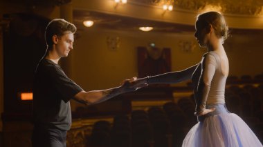 Seçkin bale dansçıları koreografi provası sırasında tiyatro sahnesinde bale hareketleri yaparlar. Erkek ve kadın pratik yapar ve dans gösterisine hazırlanırlar. Klasik bale sanatı. Dramatik ışıklandırma.
