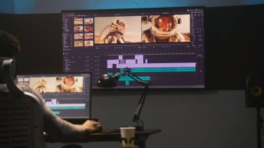 Afrikalı Amerikalı renklendirici video düzenleme yazılımında renk derecelendirme yapıyor. Uzay yolculuğu film görüntülerine ve RGB renk düzeltme çubuğuna sahip birden fazla monitör. Modern stüdyoda post prodüksiyon.