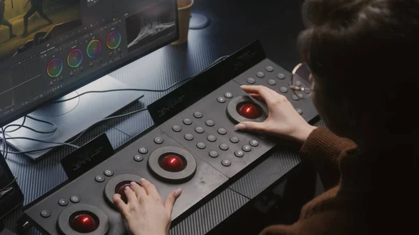 Female editor uses digital color grading control panel. Colorist makes video or photo color correction on computer in studio. Footage and program interface with RGB color wheels and levels on monitor.