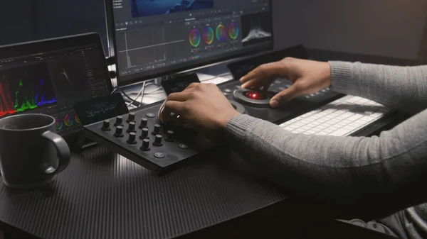 Hands close up of African American video editor working by color grading control panel in studio with modern design. Colorist makes colour correction for movie post production. Professional equipment.