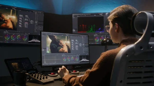 The editor works in studio on computer, uses color grading control panel, edits video, makes color correction for movie. Big screens showing program interface with film footage, RGB graphic and levels