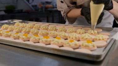 Profesyonel şekerlemeci, boru torbasıyla makarna kabuğuna ganache kremi sıkıyor ve son dokunuşları yapıyor. Lezzetli Fransız tatlısı yapma süreci. Şekerleme ve pişirme hazırlıklarını kavrayın.