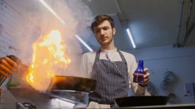 Önlüklü erkek aşçı, kızartma tavasını ateşe veriyor. Flaşlı et kızartması, gaz ocağı kullanıyor ve biber ekliyor. Gurme yemeği hazırlama süreci. Profesyonel mutfağı olan bir restoran. Gastronomik sanat.