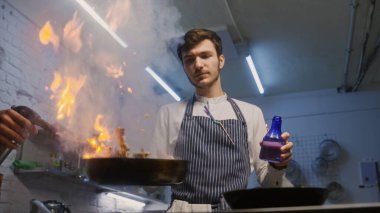 Önlüklü erkek aşçı, kızartma tavasını ateşe veriyor. Flaşlı et kızartması, gaz ocağı kullanıyor ve biber ekliyor. Gurme yemeği hazırlama süreci. Profesyonel mutfağı olan bir restoran. Gastronomik sanat.