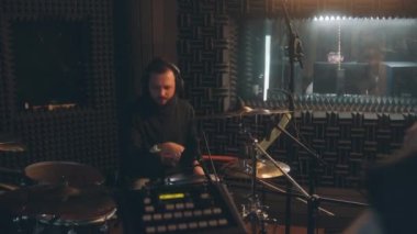 Müzik grubu ses kayıt stüdyosunda albüm için şarkı kaydediyor. Kulaklıklı erkek davulcu davul çalar. Arka planda ses mühendisi var. Müzik kayıt odasında çalış. Müzik üretim konsepti.
