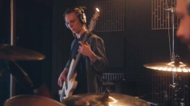 Müzik grubu ses kayıt stüdyosunda şarkı kaydediyor. Kulaklık takan erkek gitarist elektro gitar çalıyor. Davul çalan davulcuya yakın çekim. Müzik kayıt odası. Müzik üretim konsepti.