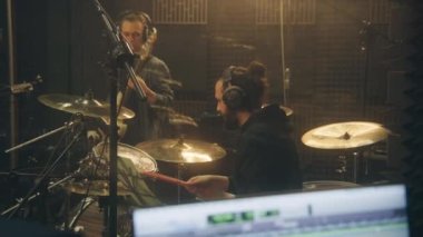 Müzik bandosu kayıt odasında şarkı kaydediyor. Bilgisayar ekranı DAW dijital ses çalışma istasyonu yazılım arayüzünü şarkı parçalarıyla gösteriyor. Profesyonel ses kayıt stüdyosu. Müzik üretimi.