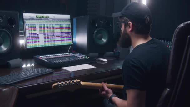 オーディオエンジニア ミュージシャンはエレクトリックギターを演奏し 新しい曲を作成するためのレコード曲 サウンドトラックとDawプログラムインターフェースを示すコンピュータ画面 録音スタジオで働く 音楽制作 — ストック動画