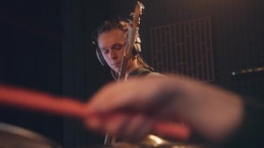 Müzik grubu ses kayıt stüdyosunda şarkı kaydediyor. Kulaklık takan erkek gitarist elektro gitar çalıyor. Baterist davul çalarken yakın çekim. Müzik kayıt odası. Müzik üretim konsepti.