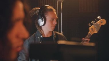 Müzik grubu ses kayıt stüdyosunda şarkı kaydediyor. Kulaklık takan erkek gitarist elektro gitar çalıyor. Şarkıcının mikrofona şarkı söylemesini kapat. Müzik kayıt odası. Müzik üretim konsepti.