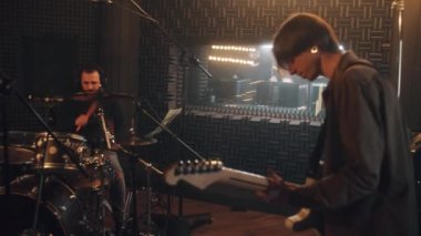 Havalı rock grubu müzik enstrümanlarıyla çalar ve ses geçirmez odada yeni albüm kaydeder. Ses mühendisi ya da yapımcı ses kayıt stüdyosundaki müzisyenlere bakar. Profesyonel müzik aletleri ve ekipmanları.