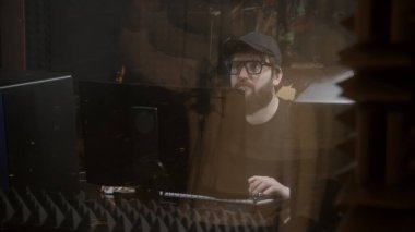 Deneyimli ses mühendisi ya da yapımcı ses kayıt stüdyosunda şarkıcıyla çalışıyor. Adam vokaliste bakar ve ses efektlerini düzenler. Bilgisayar ve karıştırma tahtası masanın üstünde. Müzik üretimi kavramı.