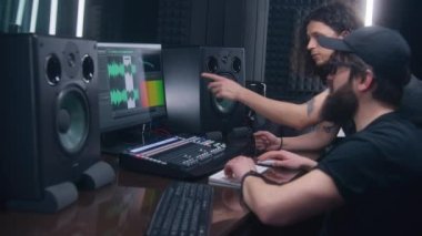 Ses mühendisi ve müzisyen müzik kayıt odasında şarkı yarattılar. Bilgisayar ekranı DAW yazılım arayüzünü ses parçasıyla gösteriyor. Ses kayıt stüdyosundaki modern ekipmanlar. Müzik üretim konsepti.